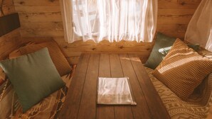A wooden cabin interior with a table, cushions, and a window with sheer curtains. - Calm Lanai Harbor (Nichinan)