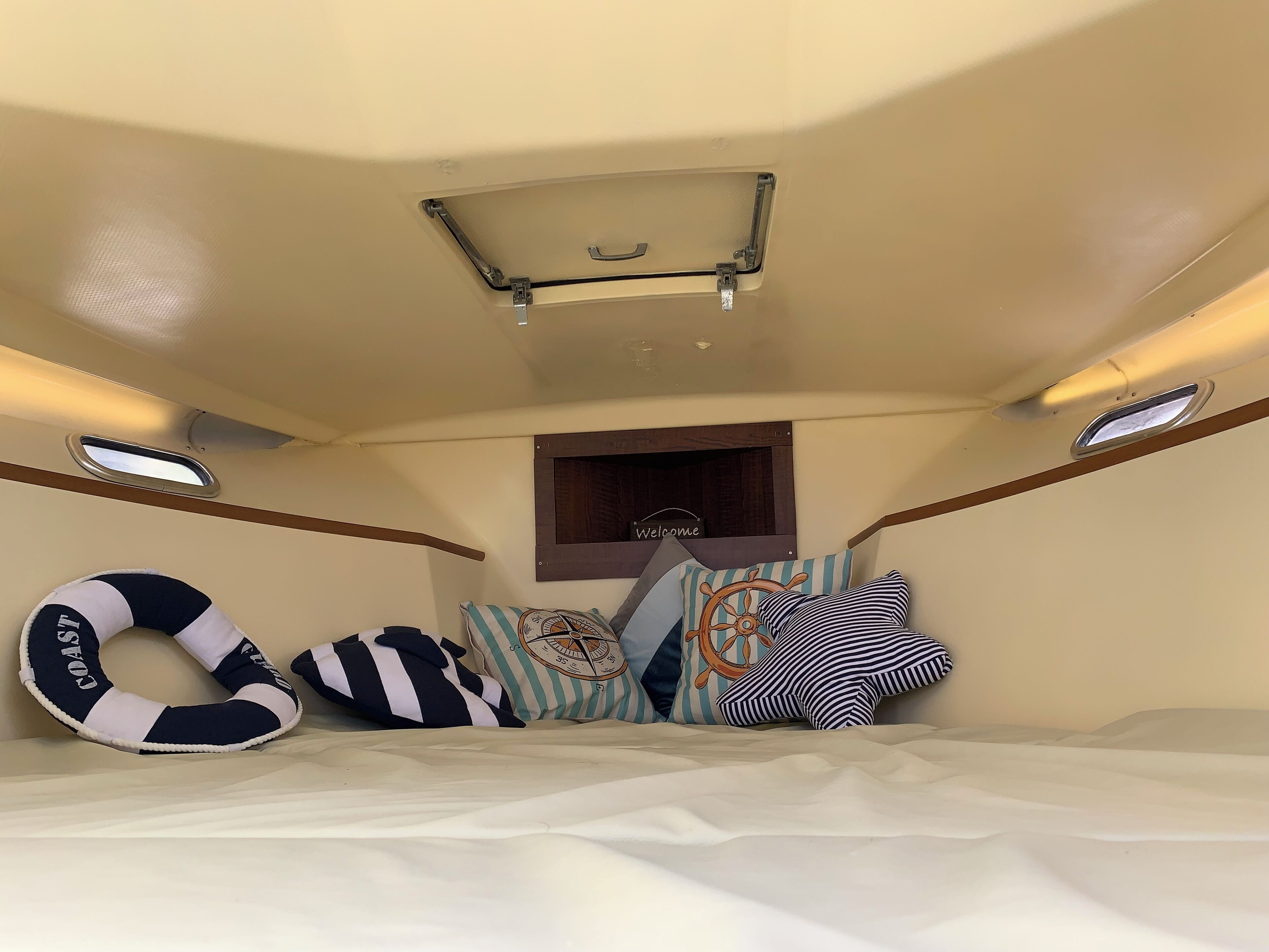 A cozy interior with a bed, pillows, a life preserver, and a 'Welcome' sign on the wall.