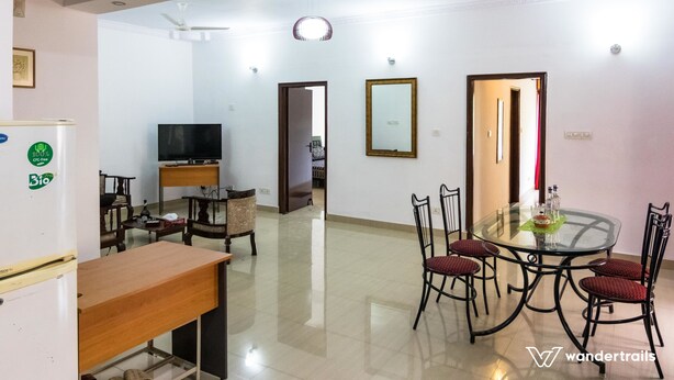 A dining area with a glass table and chairs, a refrigerator, a television, and a ceiling fan. - Luxury Apartment in Indiranagar (Bengaluru)