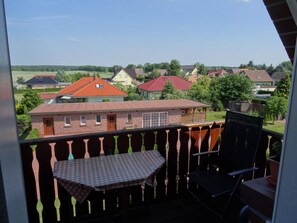 A balcony with a checkered table and chairs, overlooking a residential area with houses and greenery. - Haus Schwielochsee (Schwielochsee)