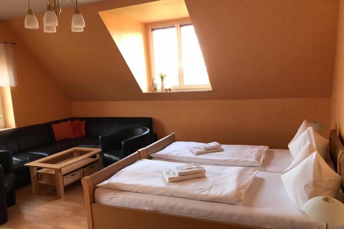 A cozy room with a sloped ceiling, a black leather sofa, two beds with white linens, and a wooden coffee table.