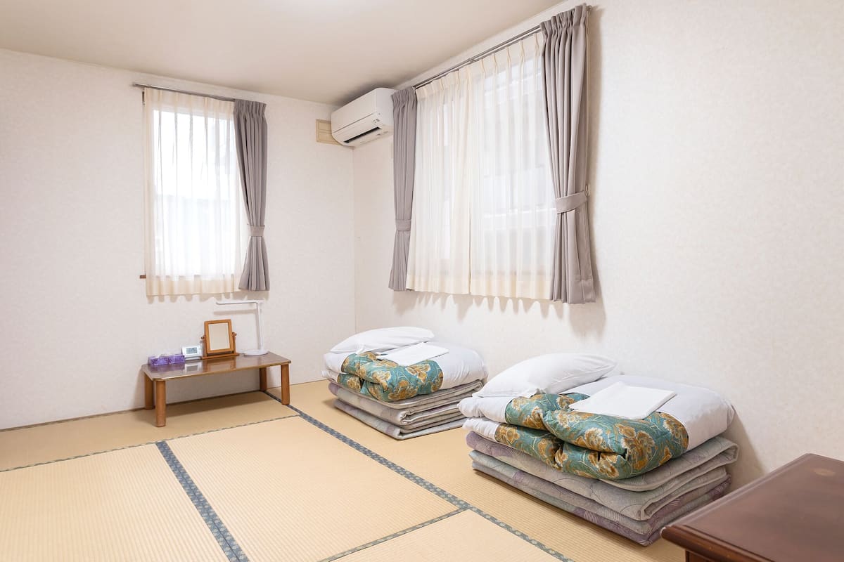 A hotel room with two beds, a TV, a small table, and an air conditioning unit.