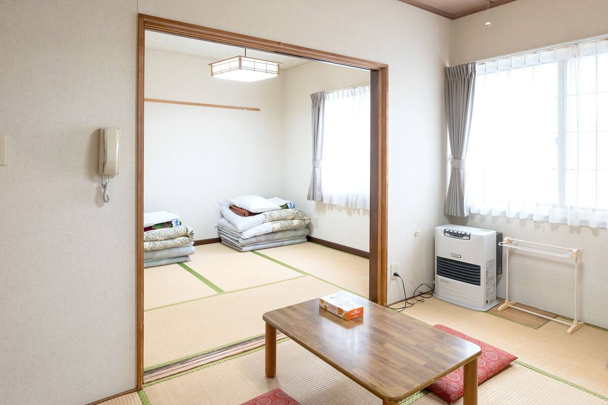 A room with tatami mats, a wooden table, a radiator, and a window with curtains.