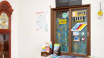 Una habitación con un reloj de pie de madera, una puerta decorada con pegatinas y una pequeña mesa con libros y revistas.