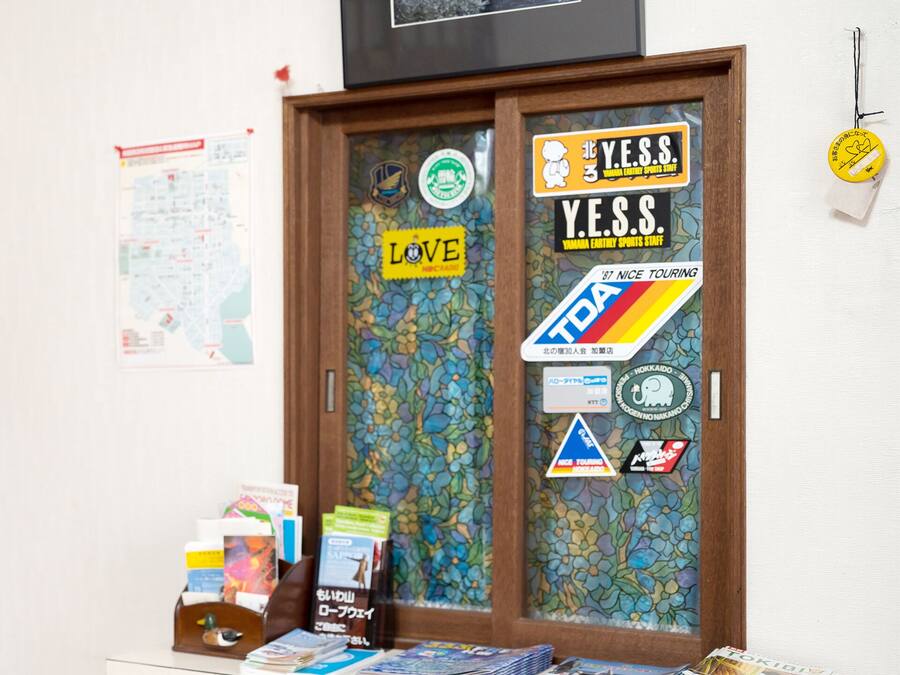 Una habitación con un reloj de pie de madera, una puerta decorada con pegatinas y una pequeña mesa con libros y revistas.