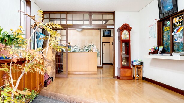 A traditional Japanese interior with wooden flooring, a reception desk, a clock, and various plants. - Pension Setsurin (Sapporo)