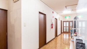 A hallway with wooden doors, a fire extinguisher, and a window with a view. - Pension Setsurin (Sapporo)