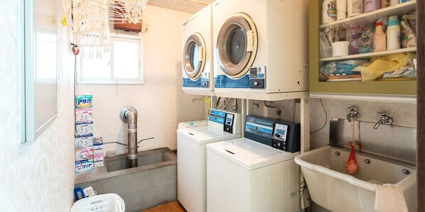 A laundry area with two washing machines, a sink, and shelves with cleaning supplies. - Pension Setsurin (Sapporo)