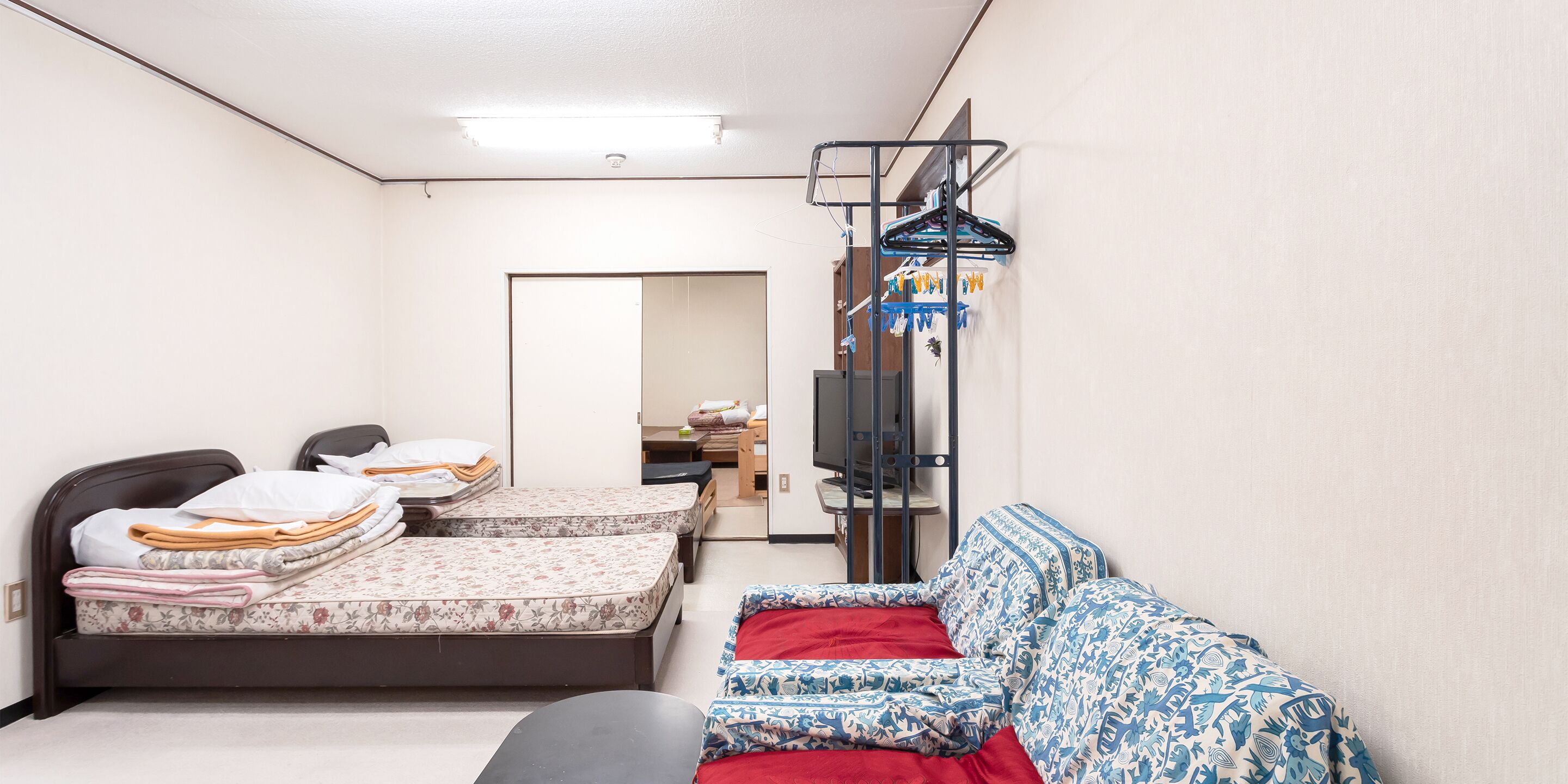 A room with two beds, a sofa, a TV, and a clothes drying rack.