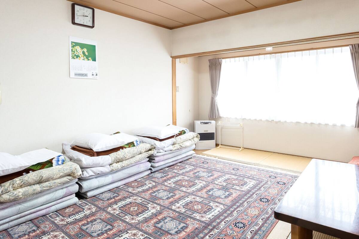A room with a bed, a desk with a computer, a window with curtains, a calendar, and a wall-mounted phone.