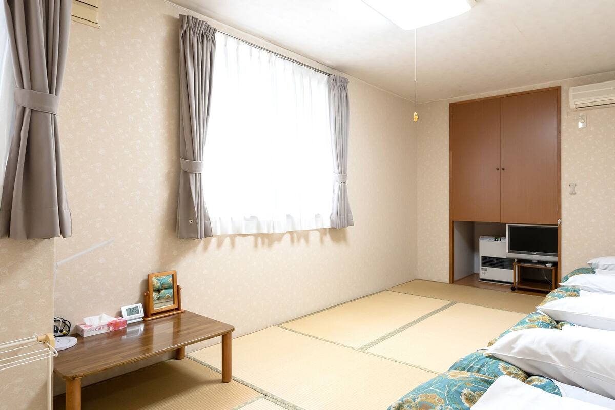 A room with tatami flooring, a futon bed, a small table with a picture frame, a heater, and a wardrobe.