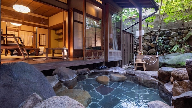 A traditional Japanese onsen with a wooden deck, stone bath, and a view of the surrounding nature.