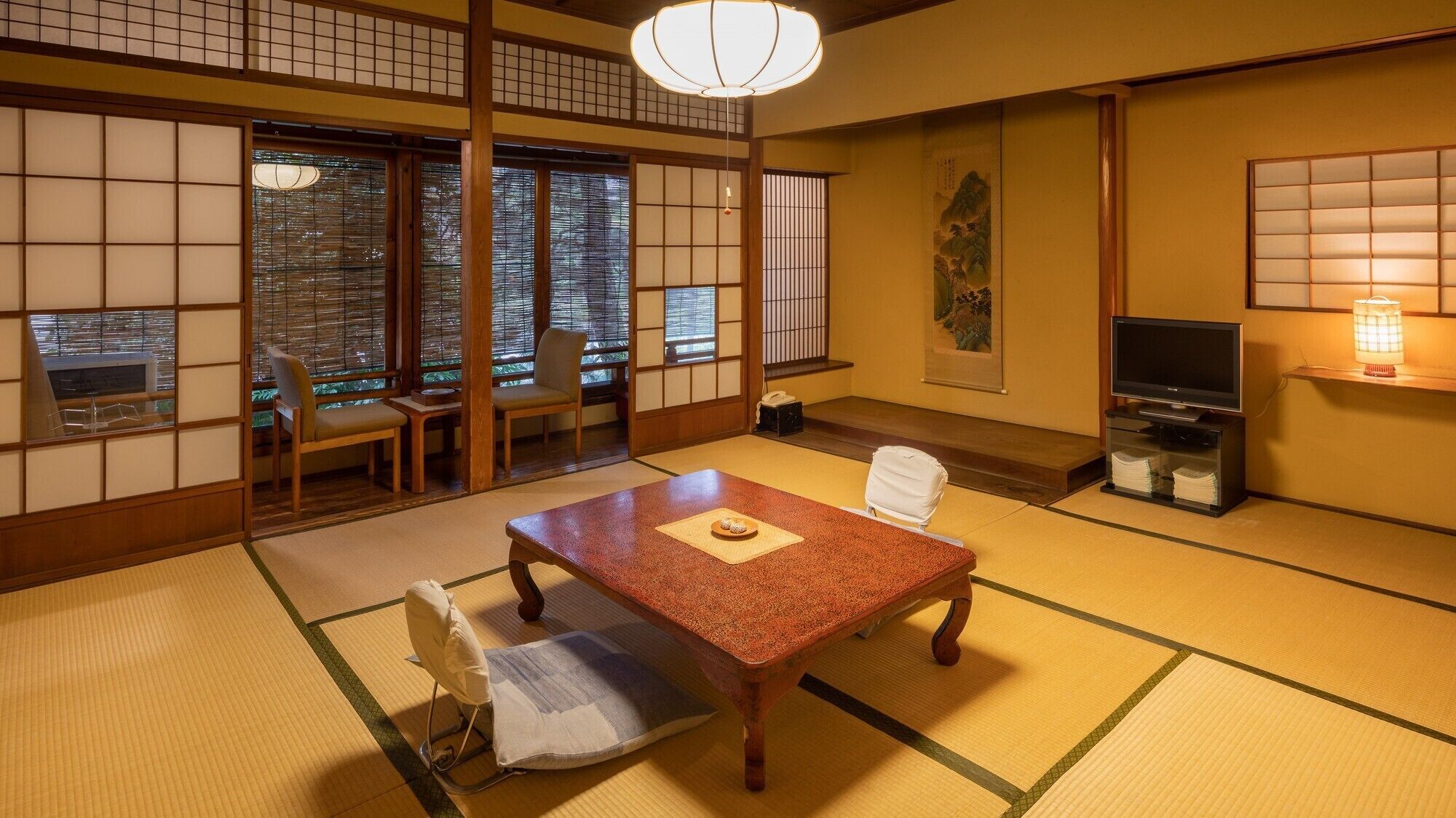 A traditional Japanese room with tatami flooring, a low table with a placemat, a television, and sliding shoji doors.