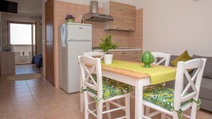 A compact kitchen with a refrigerator, a sink, and wooden cabinets. There is a dining table with chairs and a potted plant on it. - Al Faro Guest House (Vieste)