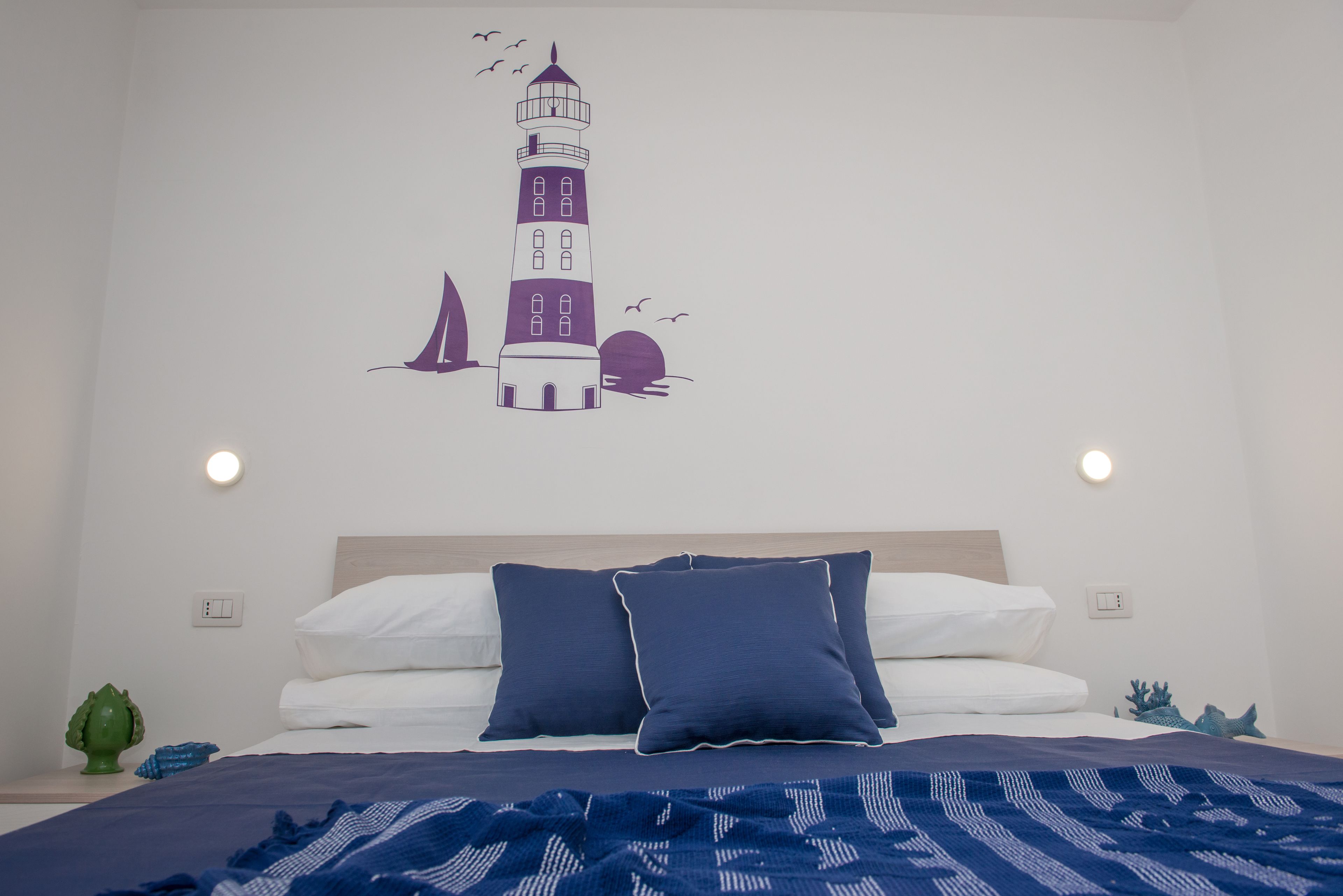 A bedroom with a bed, pillows, a wall mural, and a nightstand with a lamp.