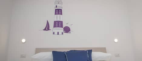 Ein Schlafzimmer mit einem Bett, Kissen, Wandbild und einem Nachttisch mit Lampe.