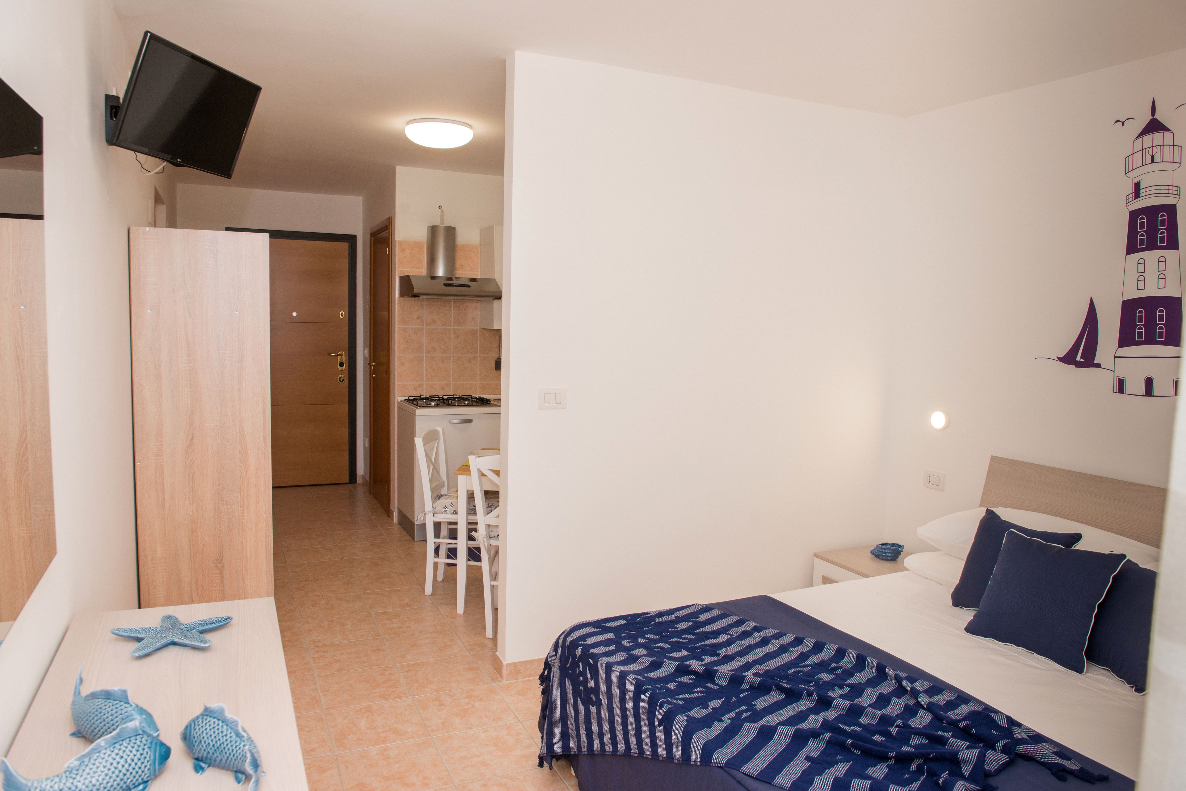 A bedroom with a bed, a desk, and a chair. There is a TV mounted on the wall.