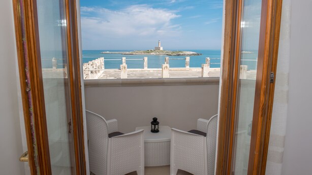 A balcony with two white wicker chairs and a small table with a lantern, overlooking a coastal view with a lighthouse. - Al Faro Guest House (Vieste)
