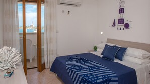 A bedroom with a bed, a nightstand, a decorative coral sculpture, a view of a lighthouse through a window, and an air conditioning unit. - Al Faro Guest House (Vieste)