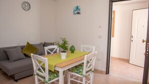 A dining area with a wooden table, white chairs, a gray sofa, and a green plant. - Al Faro Guest House (Vieste)