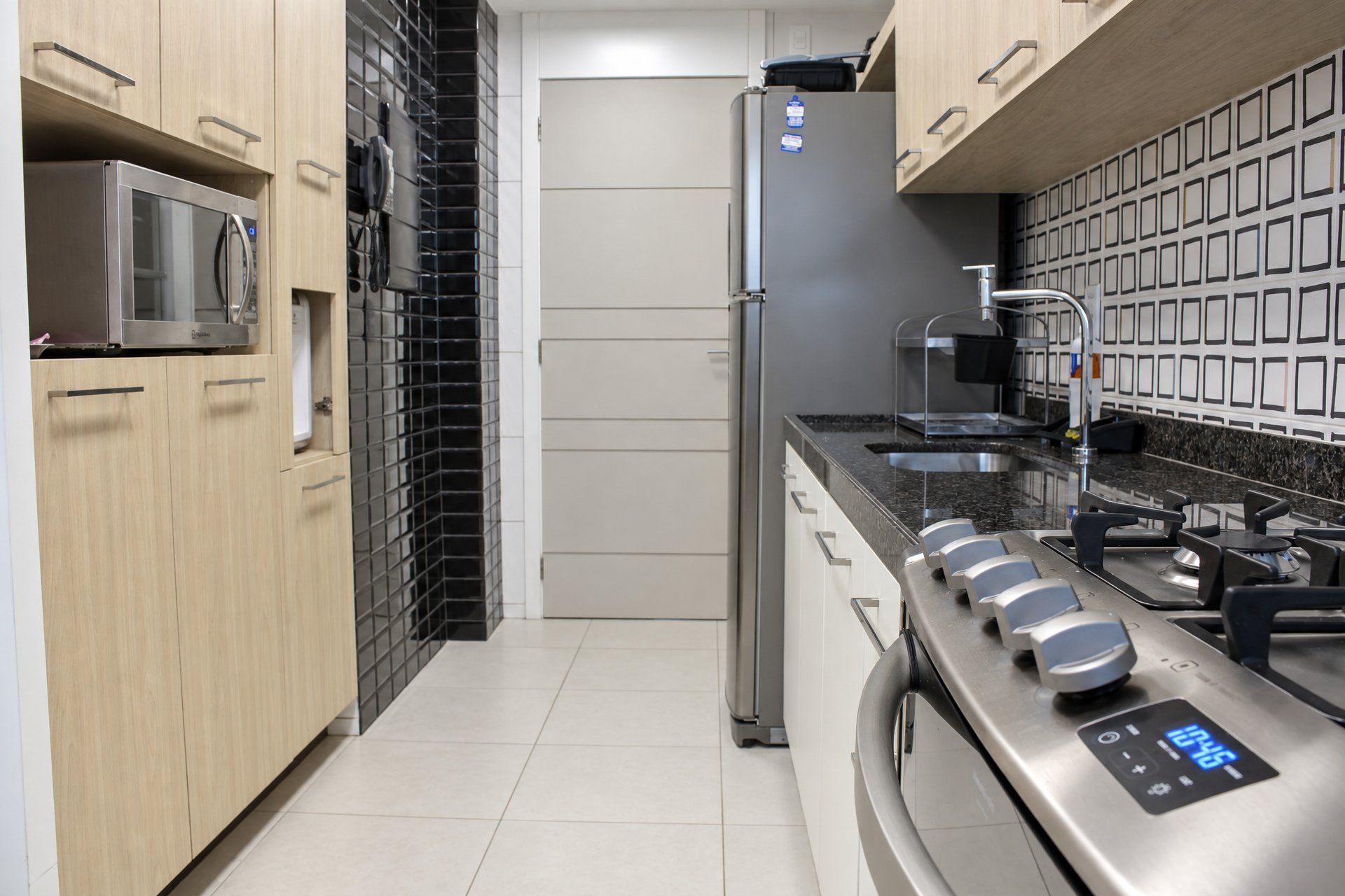 Una cocina moderna con refrigerador de acero inoxidable, microondas y horno, armarios de madera y salpicadero de azulejos.