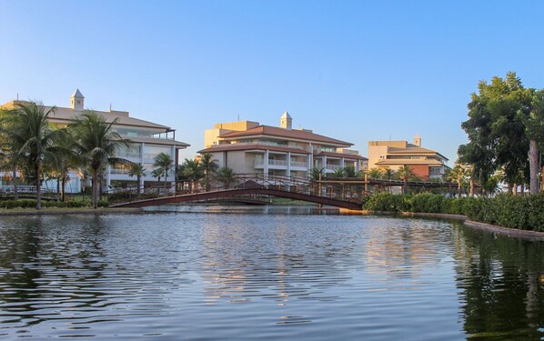 A hotel with a bridge over a calm body of water, surrounded by palm trees and other greenery. - Penthouse Apartment with Hot Tub near Beach (Aquiraz)