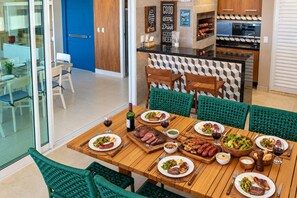 A dining area with a wooden table set for a meal, surrounded by green chairs. - Penthouse Apartment with Hot Tub near Beach (Aquiraz)