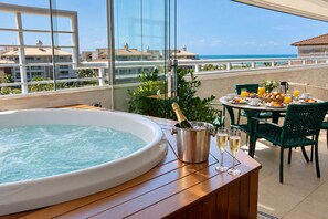 A balcony with a hot tub, dining table, chairs, and a view of the ocean. - Penthouse Apartment with Hot Tub near Beach (Aquiraz)