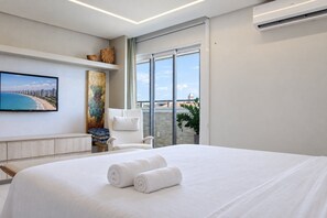 A hotel room with a bed, a television, a painting, a chair, and a view of the city through large windows. - Penthouse Apartment with Hot Tub near Beach (Aquiraz)