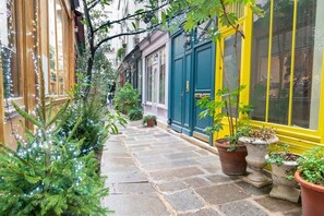 A narrow stone-paved alley with potted plants and string lights.