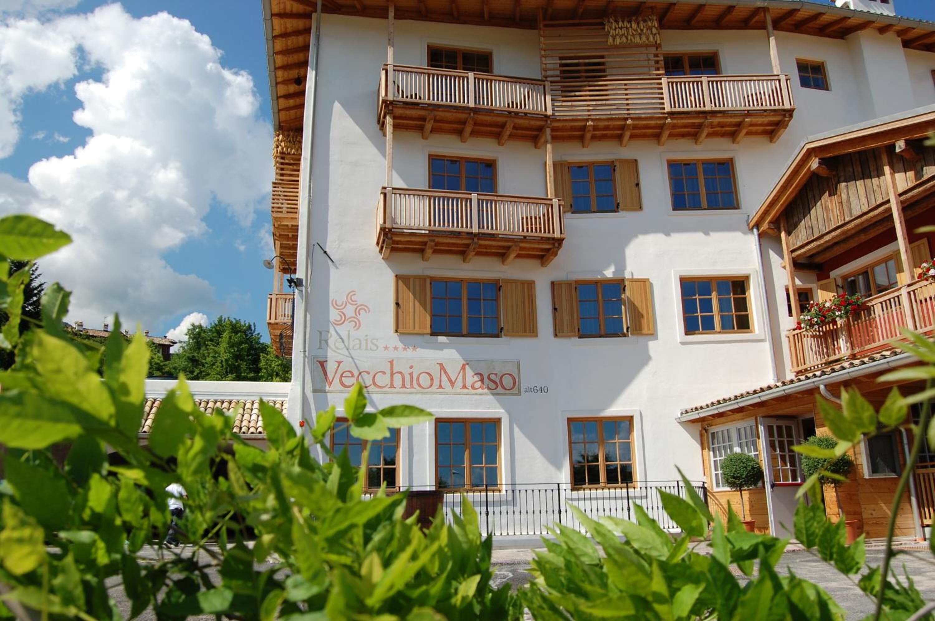 Un edificio de varios pisos con balcones, barandillas de madera y un cartel que indica que es un hotel llamado VecchioMaso.