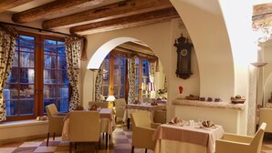 A dining area with checkered flooring, wooden beams, and floral curtains. Tables are set with tablecloths and chairs. - Relais Vecchio Maso (Trento)