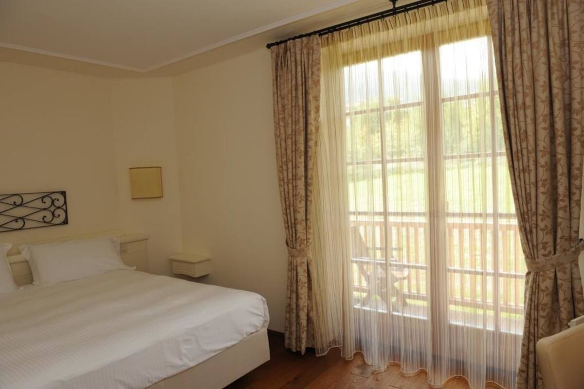 A bedroom with a bed, a nightstand, a chair, and a window with curtains.