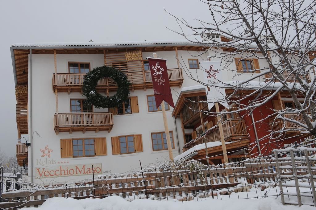 A hotel with a traditional Alpine architectural style, featuring wooden balconies and a sign for 'Relais VecchioMaso'.