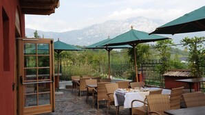 An outdoor seating area with wicker chairs and tables, green umbrellas, and a view of mountains in the background. - Relais Vecchio Maso (Trento)