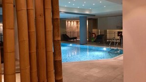 An indoor swimming pool area with a tiled floor, a seating area with chairs and a table, and a wall with a textured pattern. - Relais Vecchio Maso (Trento)