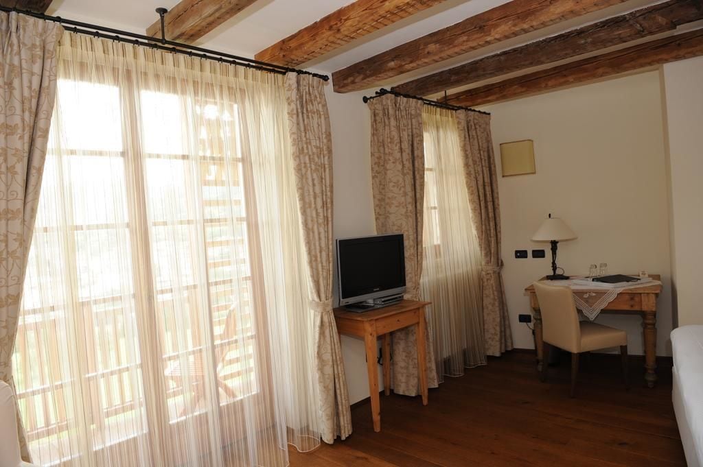 Ein Zimmer mit Holzbalken, einem Fernseher auf einem kleinen Tisch, einem Schreibtisch mit Lampe und einem Bett.