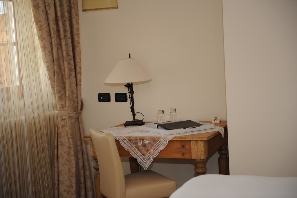 A hotel room with a wooden desk, a lamp, a chair, and a bed.