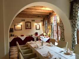 Un comedor con una larga mesa dispuesta para una comida, techo abovedado y cuadros en las paredes.