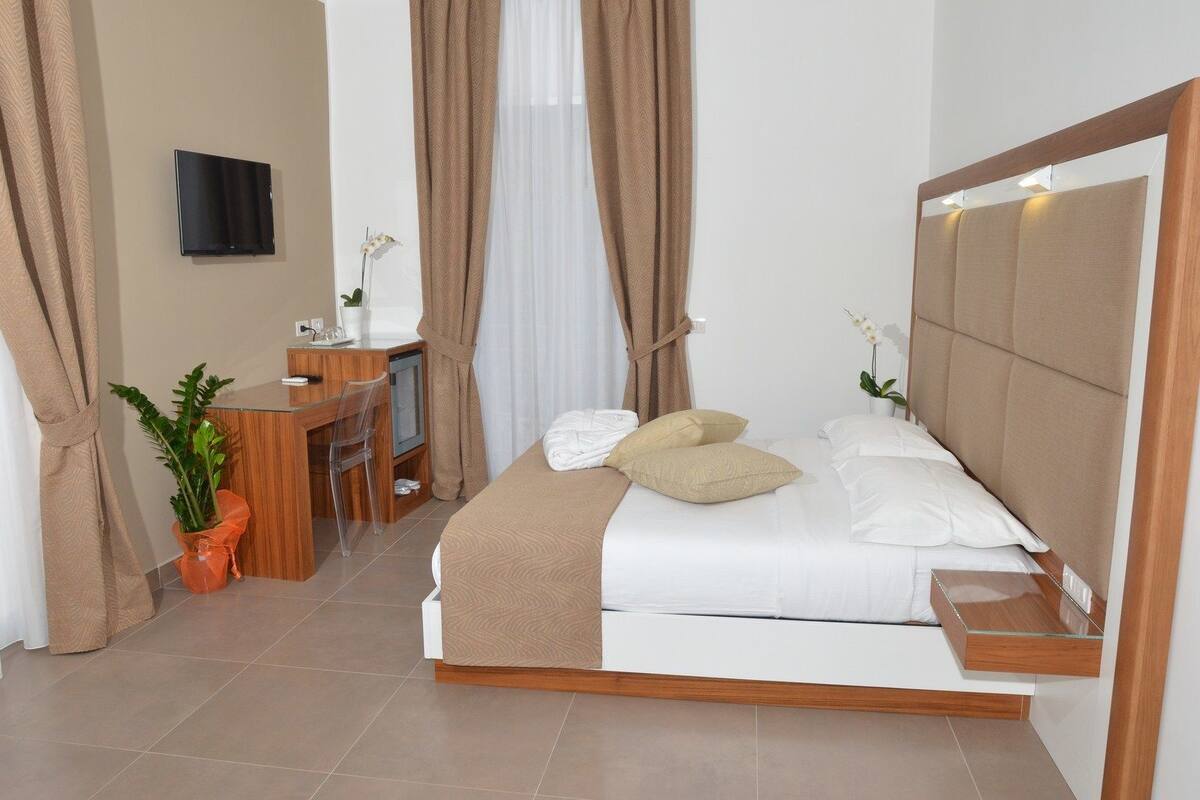 A modern hotel room with a bed, bedside table, and a desk with a chair.