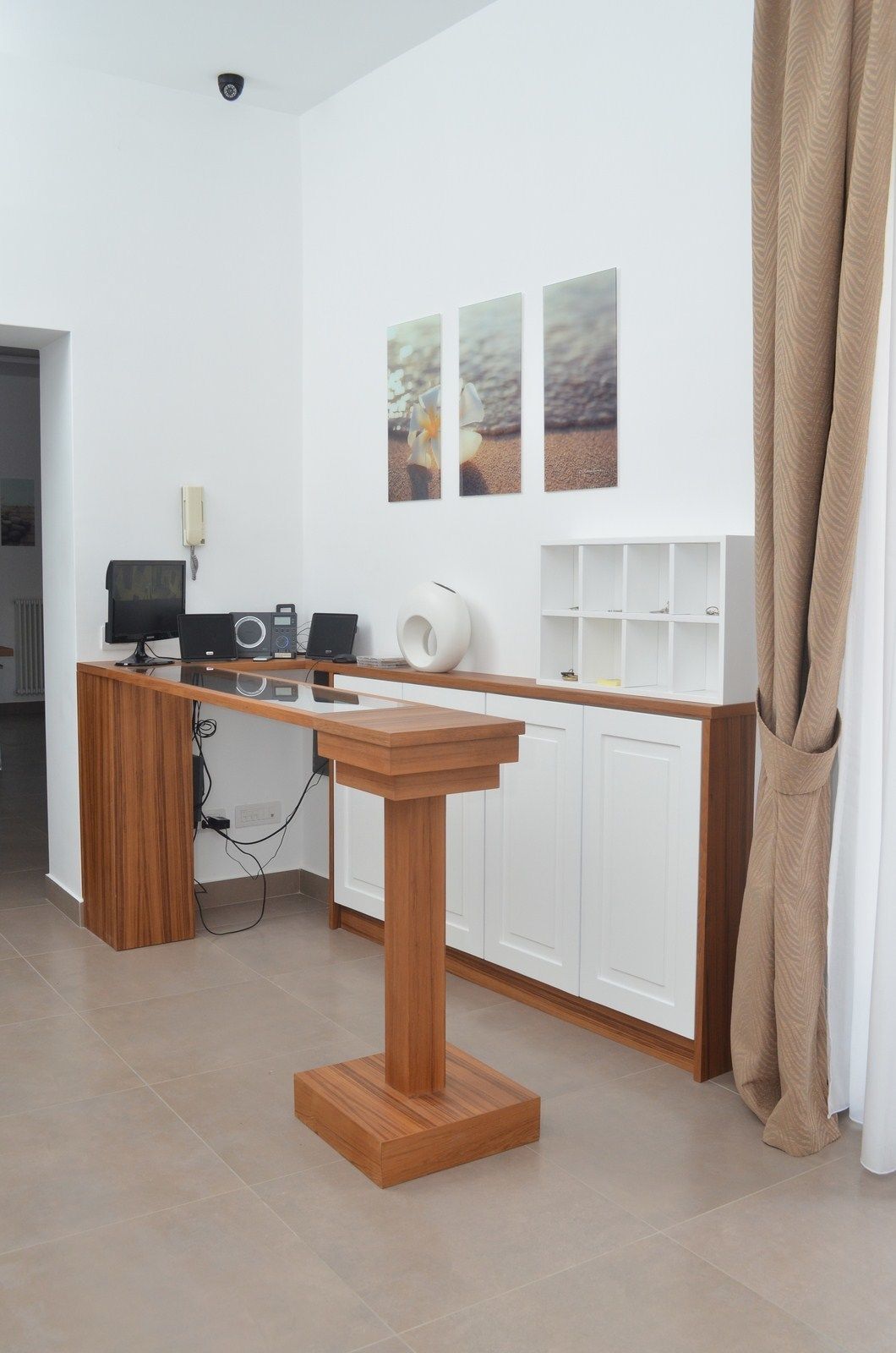 A modern kitchen with a wooden table, white cabinets, and a kitchen island. There are three framed pictures on the wall, a white vase, and a telephone on the wall.
