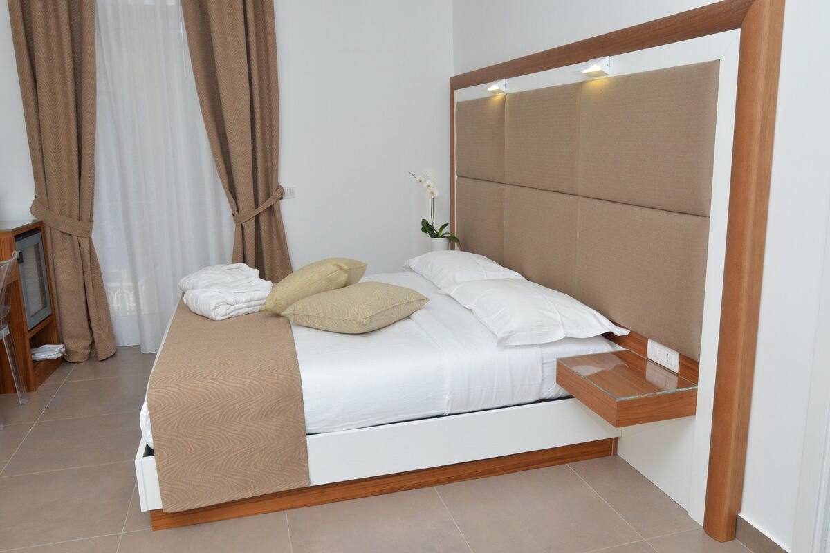 A neatly made bed with white and beige bedding, a wooden headboard, and a bedside table with a glass top.