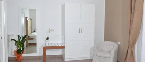 A room with a bed, a white wardrobe, a bench, a chair, and a potted plant.