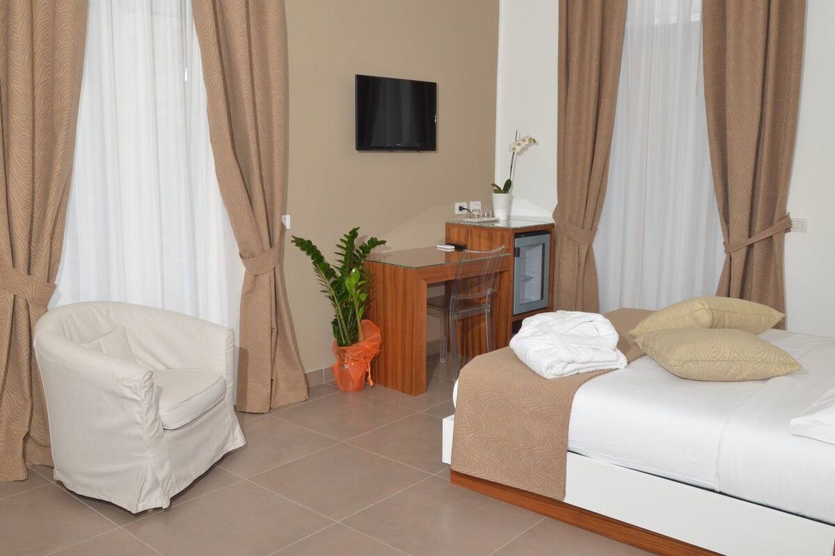 A hotel room with a bed, a desk, a chair, and a potted plant.