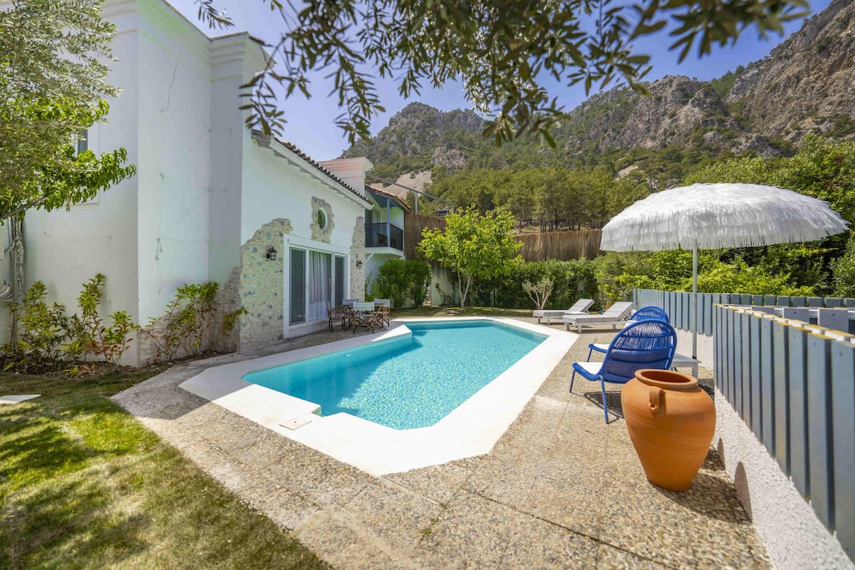 Une piscine dont le bord est recouvert de carreaux blancs, une chaise bleue et un grand pot en terre cuite.