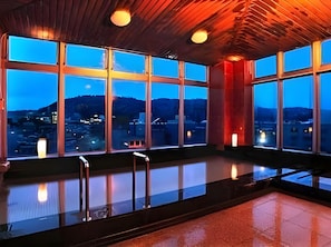 A spacious indoor area with large windows offering a view of a cityscape at dusk. - Hotel Ark 21 (Kurayoshi)
