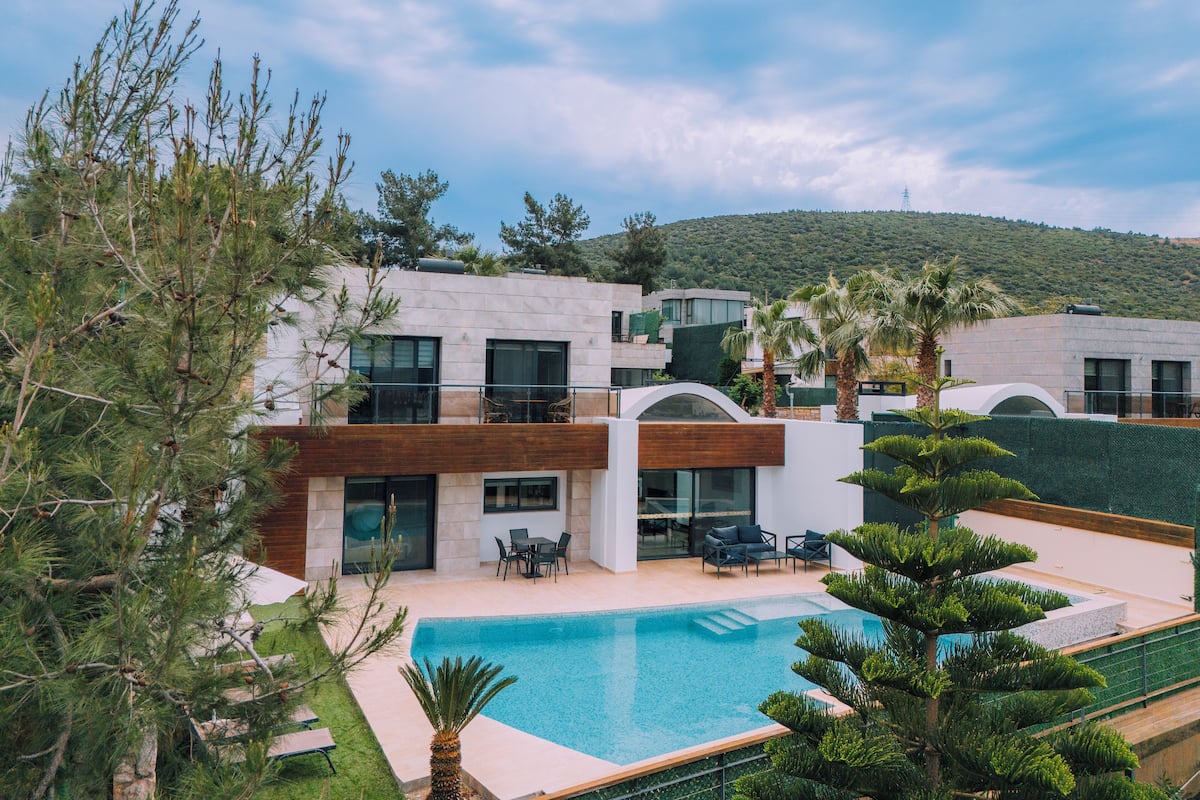Un edificio moderno de varios pisos con piscina, mobiliario exterior y abundante vegetación.