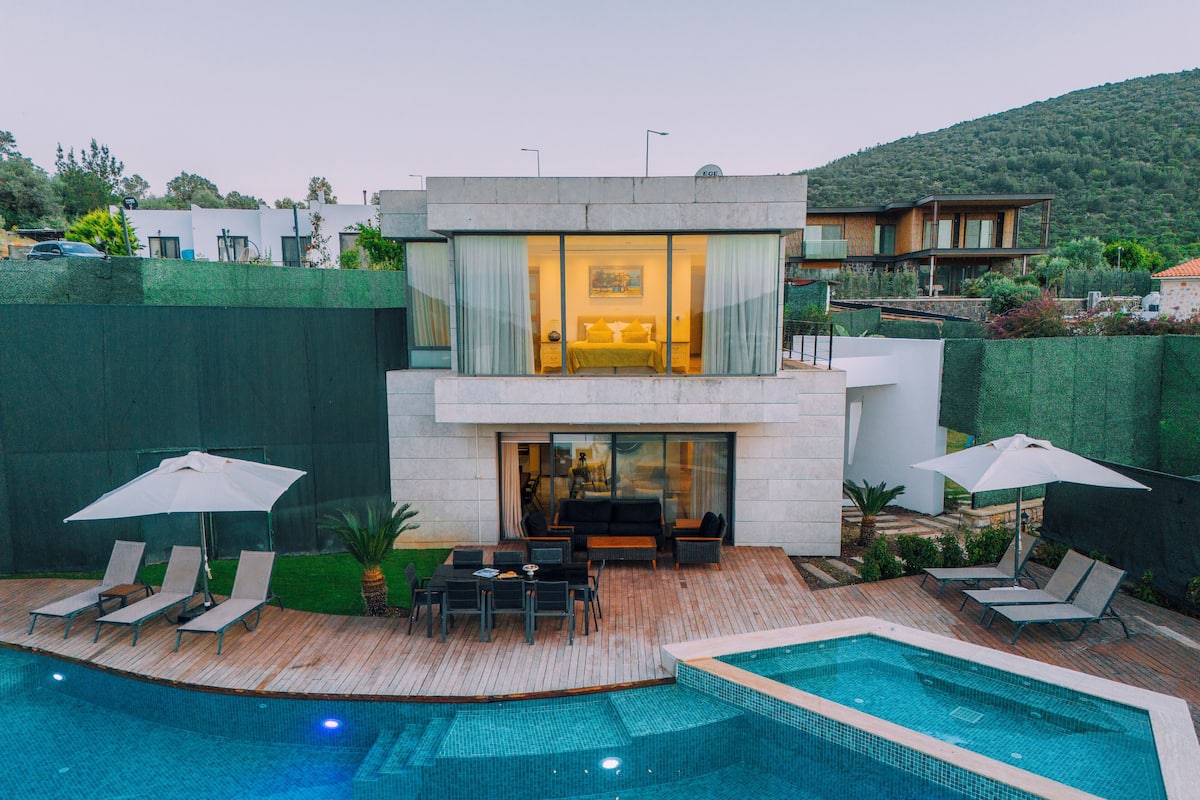 Una casa moderna de dos pisos con piscina, mobiliario exterior y vistas del paisaje circundante.