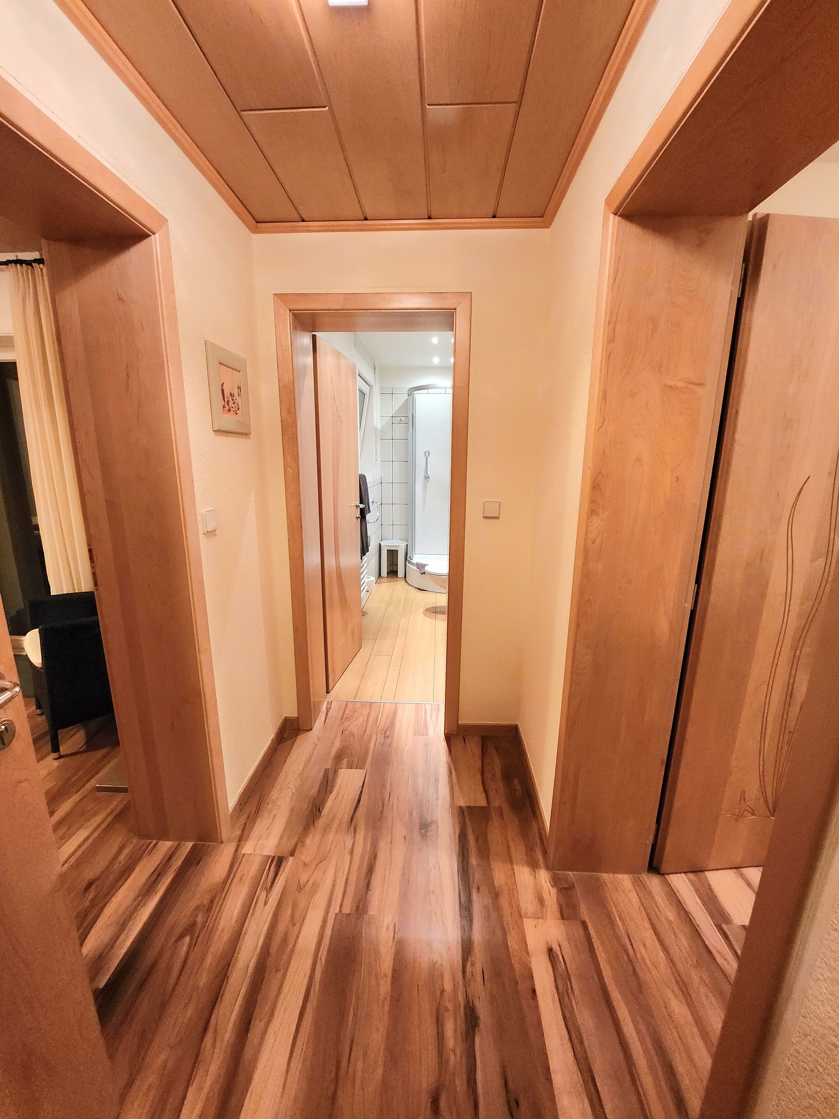 A hallway with wooden flooring and doors leading to a bathroom and a kitchen.