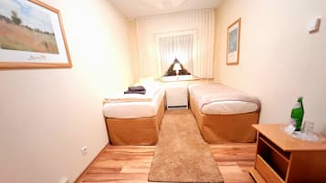 Una habitación de hotel estrecha con dos camas individuales, una mesita pequeña y una mesita de noche.
